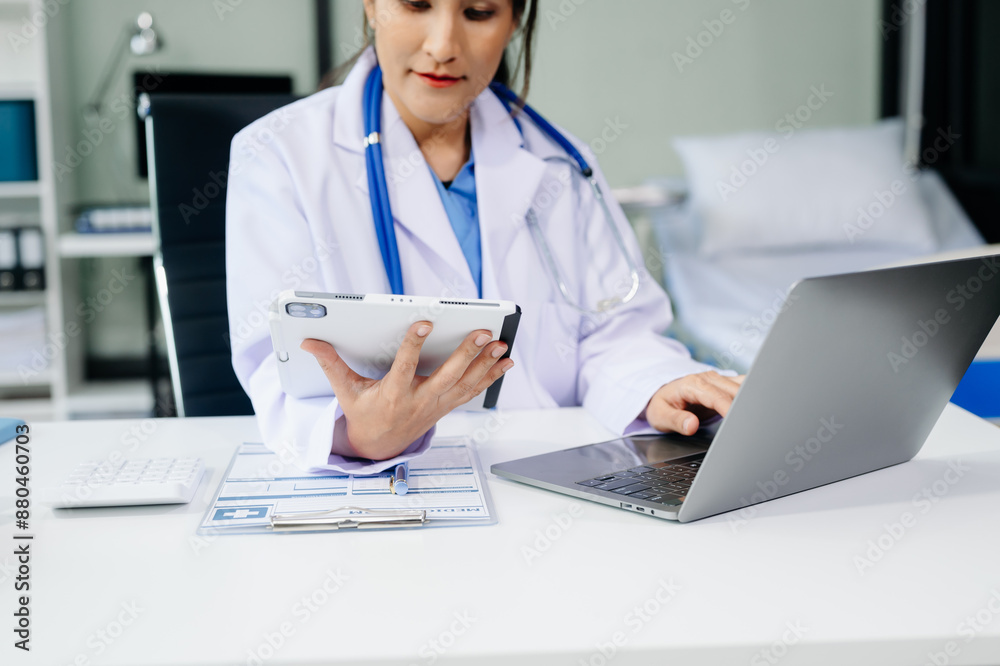 Beautiful physician doctor sit on table in office hospital. Attractive therapist female practitioner pharmacist smile and use tablet and laptop. Beautiful physician doctor sit on table in office hospital. Attractive therapist female practitioner pharmacist smile and use tablet and laptop.