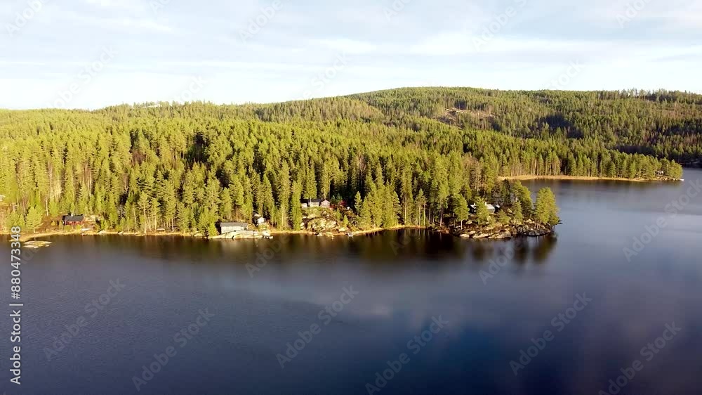 Aerial view of a serene lake surrounded by a dense Norwegian forest with scattered cabins along the shoreline, bathed in soft sunlight. Aerial view of a serene lake surrounded by a dense Norwegian forest with scattered cabins along the shoreline, bathed in soft sunlight.