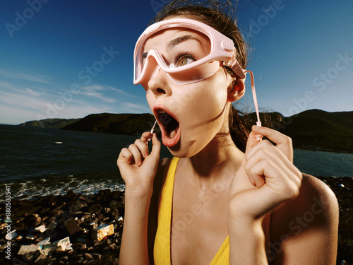 Woman in yellow swimsuit with wide open mouth and eyes holding goggles in front of her face, expressing surprise or excitement