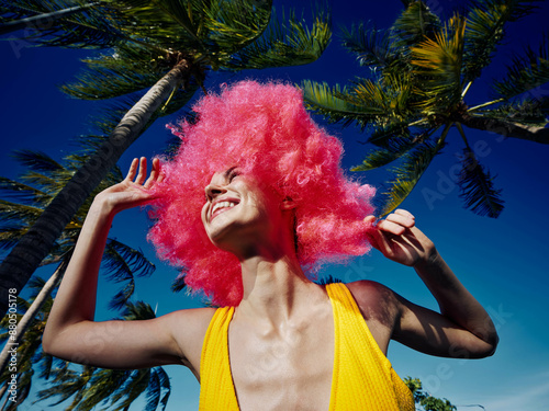 Bright pinkhaired woman standing in front of a palm tree, her vibrant locks flowing in the wind, creating a dynamic and lively scene photo