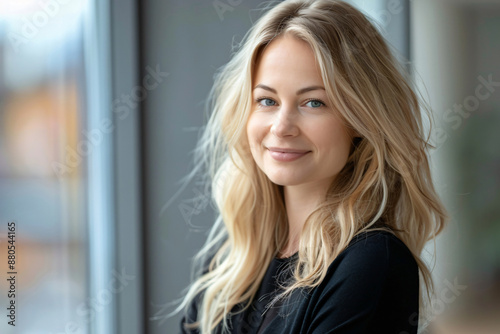 Free Download Close up portrait of beautiful smiling blonde business woman in casual looking at camera while standing against window, blurred background with office interior. - GFXLoad