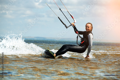 Smiling woman with a kiteboard looks at the camera while sailing through the waves on a parachute, kite. Fast travel with a wave from the board