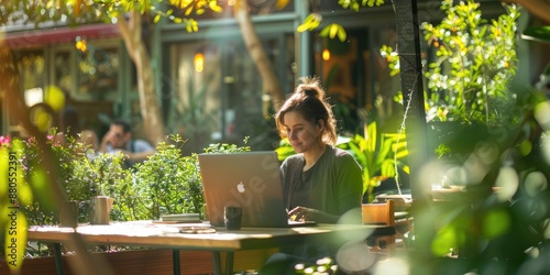 A person is using a laptop in a tranquil outdoor cafe surrounded by plants, bathed in natural sunlight AIG58 photo