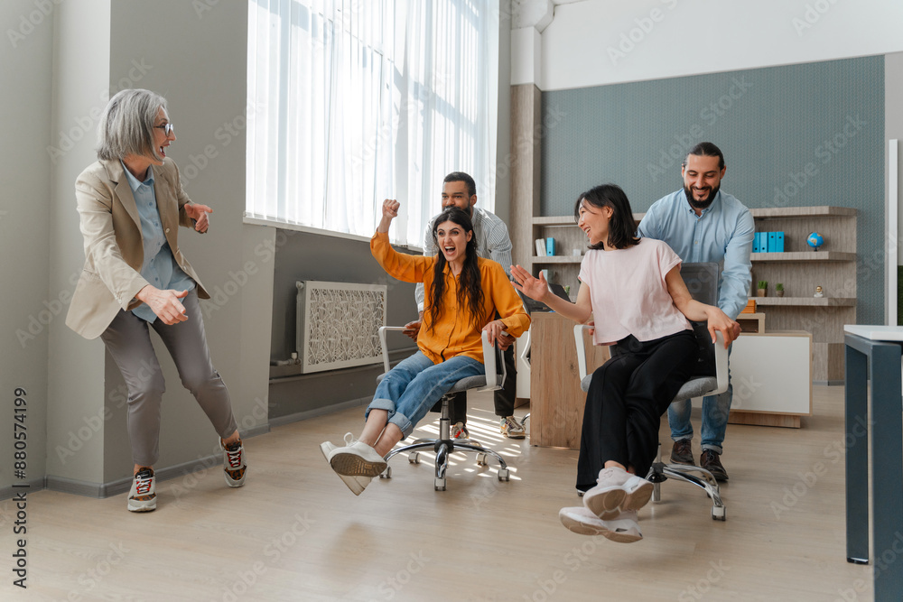 Happy business team having fun racing on chairs in office Happy business team having fun racing on chairs in office