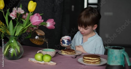 Little boy adorable having breakfast with pancakes with tea and apples at home. Cute weekend with sweet tasty food and emotional child. video footage 4k
