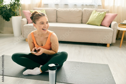 Middle-aged woman sits on yoga mat, holding cell phone. © LIGHTFIELD STUDIOS