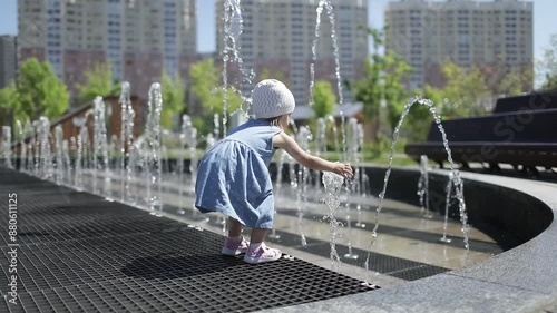 A little girl plays with a fountain on a hot sunny day in summer.