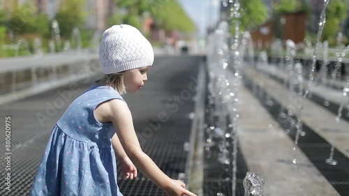 A little girl plays with a fountain on a hot sunny day in summer. Funny moment with a child.