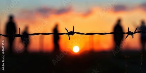 Barbed wire fence in silhouette against the background of sunset sky, close-up. The concept of security and prison, border control, and protection from commerce.