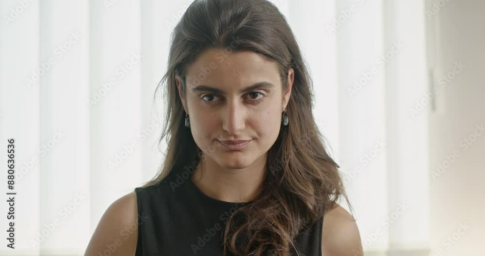 Young businesswoman taking a deep breath in office setting, wearing black sleeveless top, looking serious and stressed.