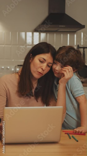 Vertical screen: Child seeks attention from mother who is working on laptop at kitchen. Concept of balancing work and family responsibilities. Multitasking and parental involvement