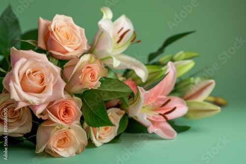 A mixed arrangement of peach roses and pink lilies with green leaves lies on a green background. The flowers are in soft focus, creating a romantic and delicate aesthetic photo