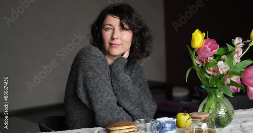 Positive middle age women sitting the the table at home with tea and pancakes. Beautiful lade looking at the camera, smiling, wearing casual clothing. video footage 4k