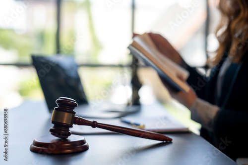 Fotografie A woman is reading a book while sitting at a desk with a gavel and a laptop