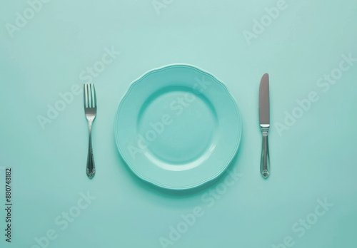 An overhead shot of a mint-colored plate centered between a fork and knife, arranged symmetrically on a matching mint-colored background. photo