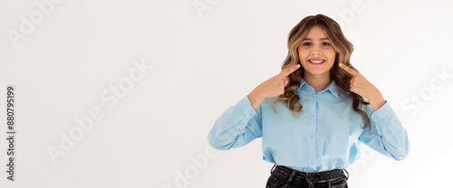 Young woman pointing fingers at her cheeks isolated over white background