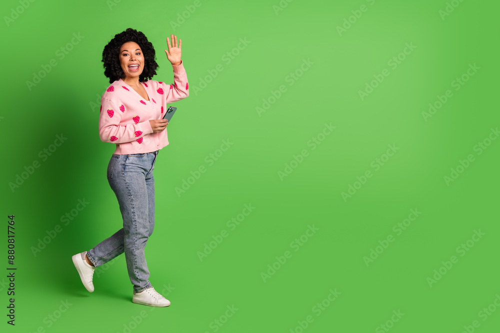 Full body photo of attractive young woman hold device walk wave hand dressed strawberry print clothes isolated on green color background Full body photo of attractive young woman hold device walk wave hand dressed strawberry print clothes isolated on green color background