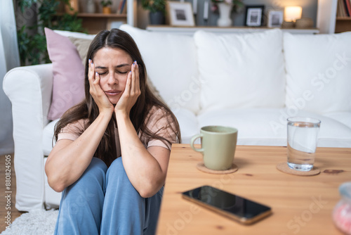 Young depressed sad anxious and worried woman sitting alone on the floor waiting for phone call from hospital. Sick stressed woman expecting medical results from doctor. Health care and medicine