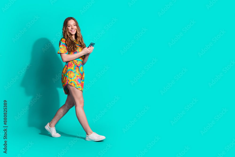 Full size photo of pretty teen girl hold device walking wear trendy colorful outfit isolated on aquamarine color background Full size photo of pretty teen girl hold device walking wear trendy colorful outfit isolated on aquamarine color background
