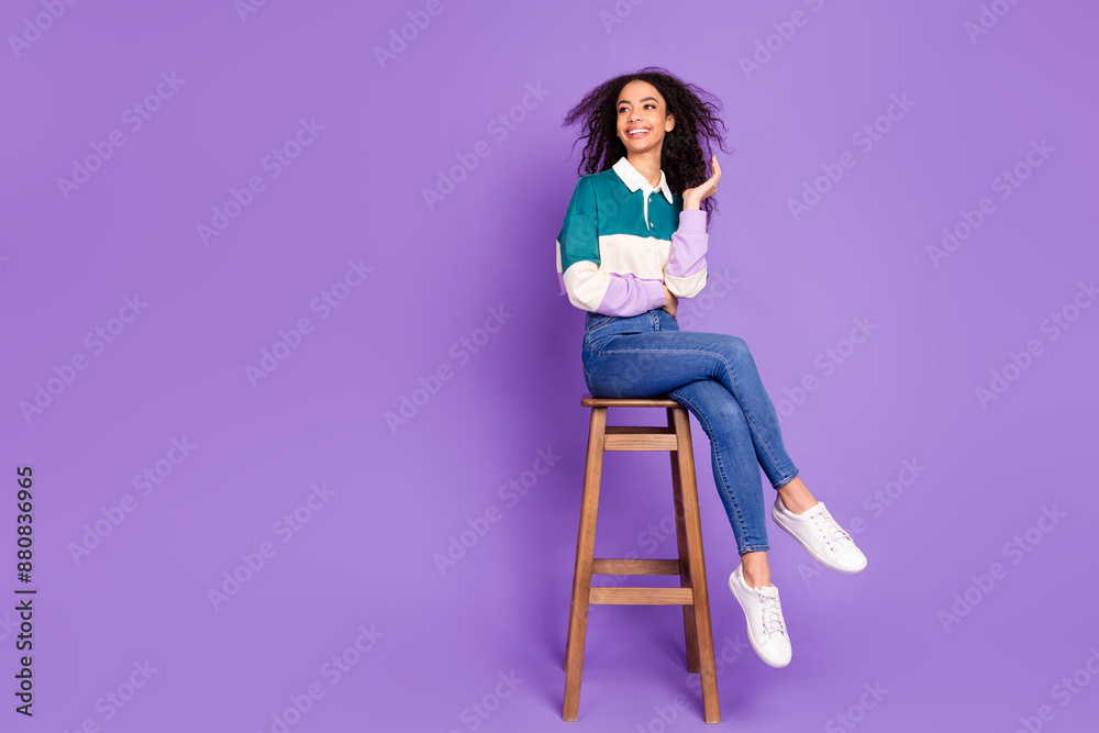 Full body portrait of lovely young girl sit stool look empty space wear shirt isolated on purple color background Full body portrait of lovely young girl sit stool look empty space wear shirt isolated on purple color background