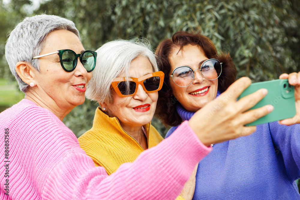 Three middle age women taking selfie in park, wearing colorful and sunglasses. Cute elderly friends having fun together outdoors. Three middle age women taking selfie in park, wearing colorful and sunglasses. Cute elderly friends having fun together outdoors.