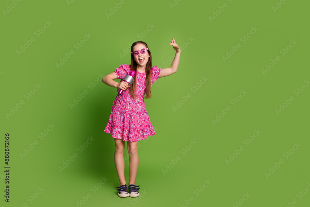 Full size photo of cute schoolgirl sing mic empty space wear pink dress isolated on green color background Full size photo of cute schoolgirl sing mic empty space wear pink dress isolated on green color background