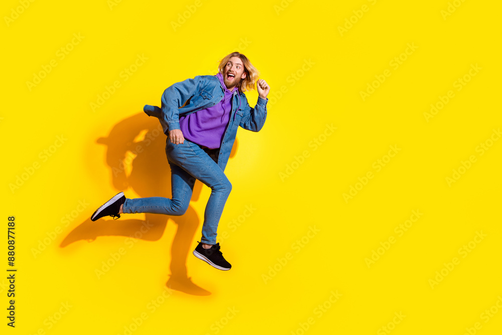 Full size photo of nice young man jump run empty space wear denim jacket isolated on yellow color background Full size photo of nice young man jump run empty space wear denim jacket isolated on yellow color background