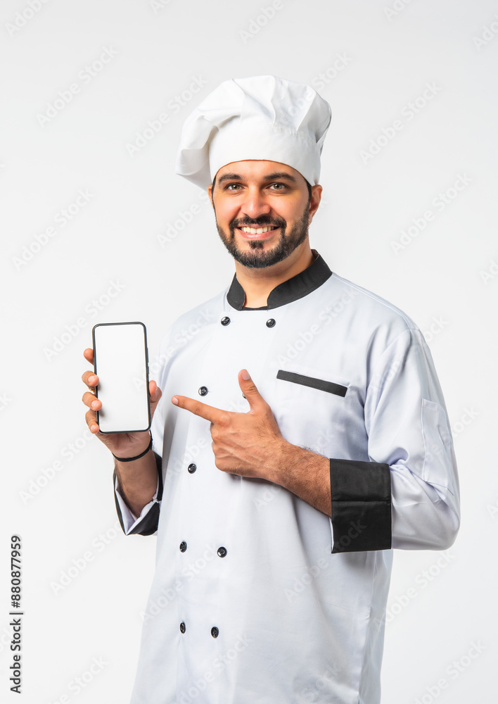 Indian Asian young chef in uniform presenting empty smartphone and white plate on white background Indian Asian young chef in uniform presenting empty smartphone and white plate on white background