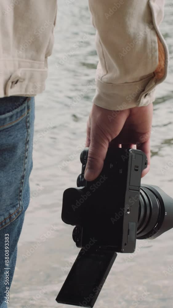 Close up vertical footage of professional video camera swaying in the videographer's hands against the background of river waves.