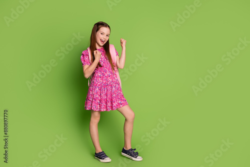 Full size photo of cute schoolgirl raise fist hold bag wear pink dress isolated on green color background