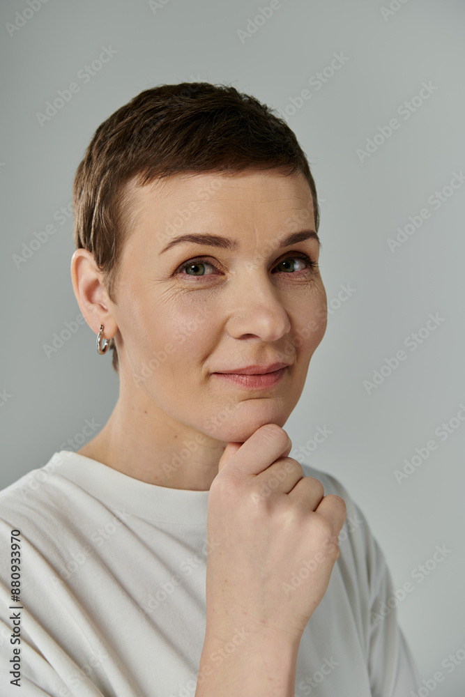 A woman with short hair, signifying breast cancer awareness, poses against a grey background. A woman with short hair, signifying breast cancer awareness, poses against a grey background.