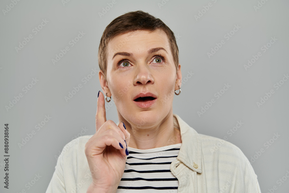 A woman with short hair and a surprised expression holds her finger up as if she has just had a great idea. A woman with short hair and a surprised expression holds her finger up as if she has just had a great idea.