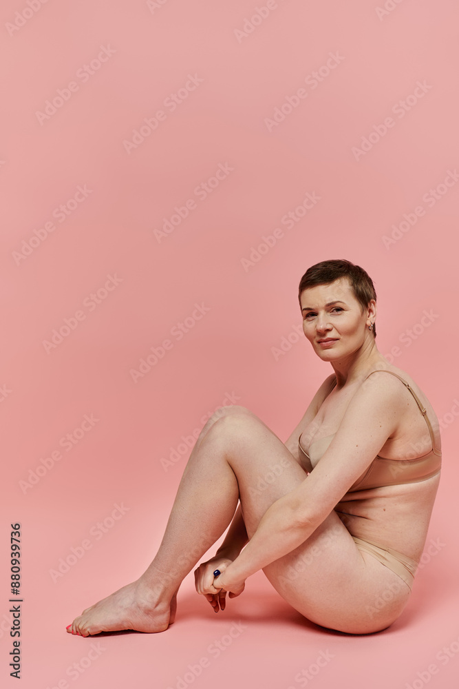 A woman with short hair sits on a pink background A woman with short hair sits on a pink background