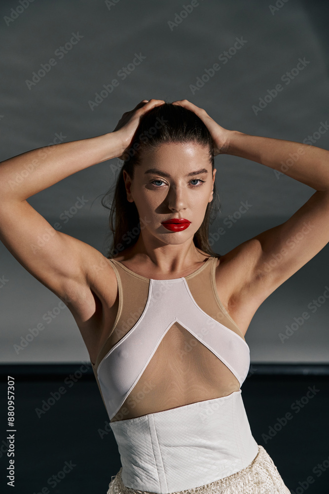 A young woman with long dark hair and red lipstick poses against a gray backdrop, wearing a white top and skirt. A young woman with long dark hair and red lipstick poses against a gray backdrop, wearing a white top and skirt.