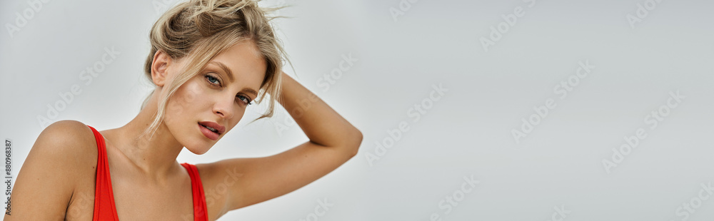 A young blonde woman in an orange swimsuit poses against a grey background, showcasing summer fashion trends. A young blonde woman in an orange swimsuit poses against a grey background, showcasing summer fashion trends.