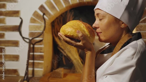 Young female woman chef-cooker holding a loaf of freshly baked bread in his hands smells the aroma of fresh bread