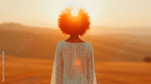 Young woman is standing in a field with her back to the camera, enjoying the warm glow of the setting sun over the tuscan hills