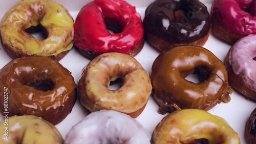 Donuts with different red, pink, chocolate icing lie in a white box, close-up top view