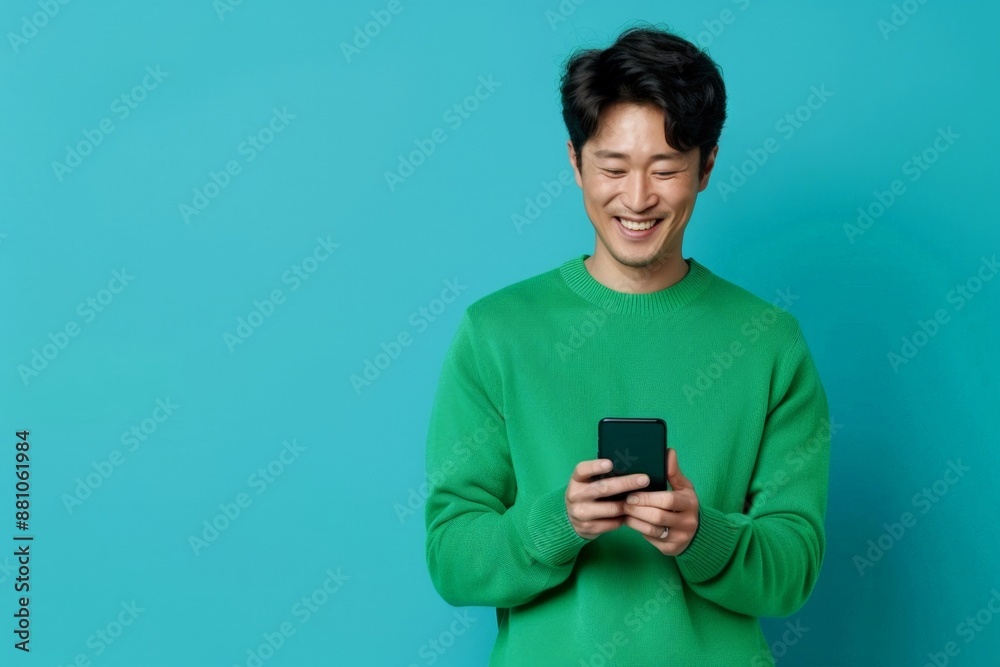 Cheerful Young Asian Man Enjoying Smartphone on Blue Background. Horizontal banner with copy space Cheerful Young Asian Man Enjoying Smartphone on Blue Background. Horizontal banner with copy space