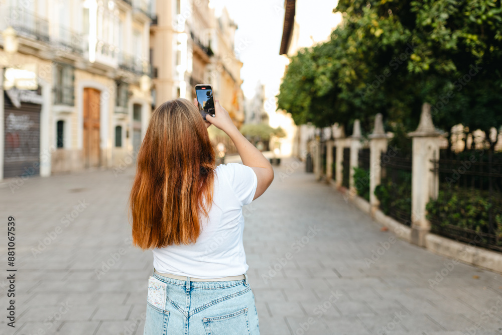 Redhead female traveler in casual dress taking picture of city street with smartphone, travel in Europe. Attractive female tourist is exploring new city. Hight quality photo