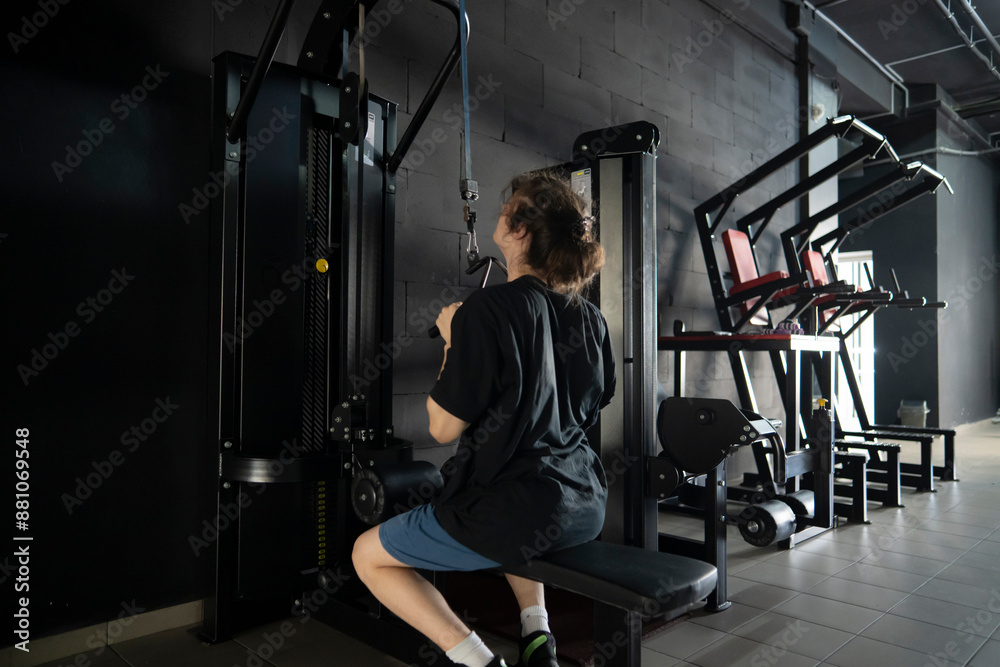 A man performs a lat pulldown exercise on a cable machine in a modern dark gym A man performs a lat pulldown exercise on a cable machine in a modern dark gym
