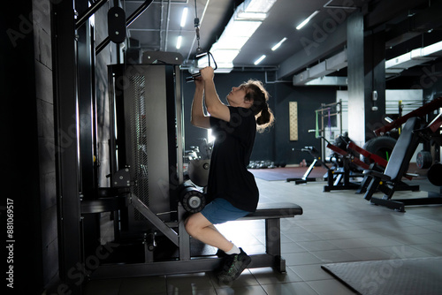 A man performs a lat pulldown exercise on a cable machine in a modern dark gym