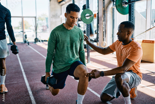 Instructor giving encouragement to a fit young man working out with dumbbells during a strength training session in a gym