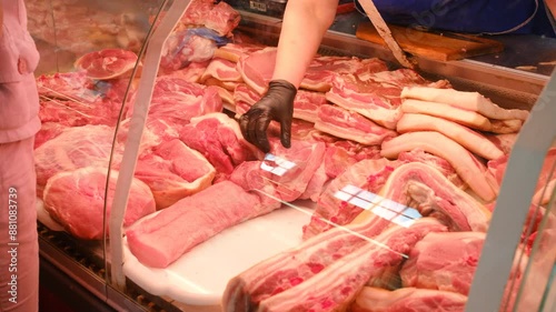 Refrigerator in a store with a pile of raw meat goods in a butcher shop with a seller and a buyer. Meat department with raw fresh meat for sale, garnished with vegetables.