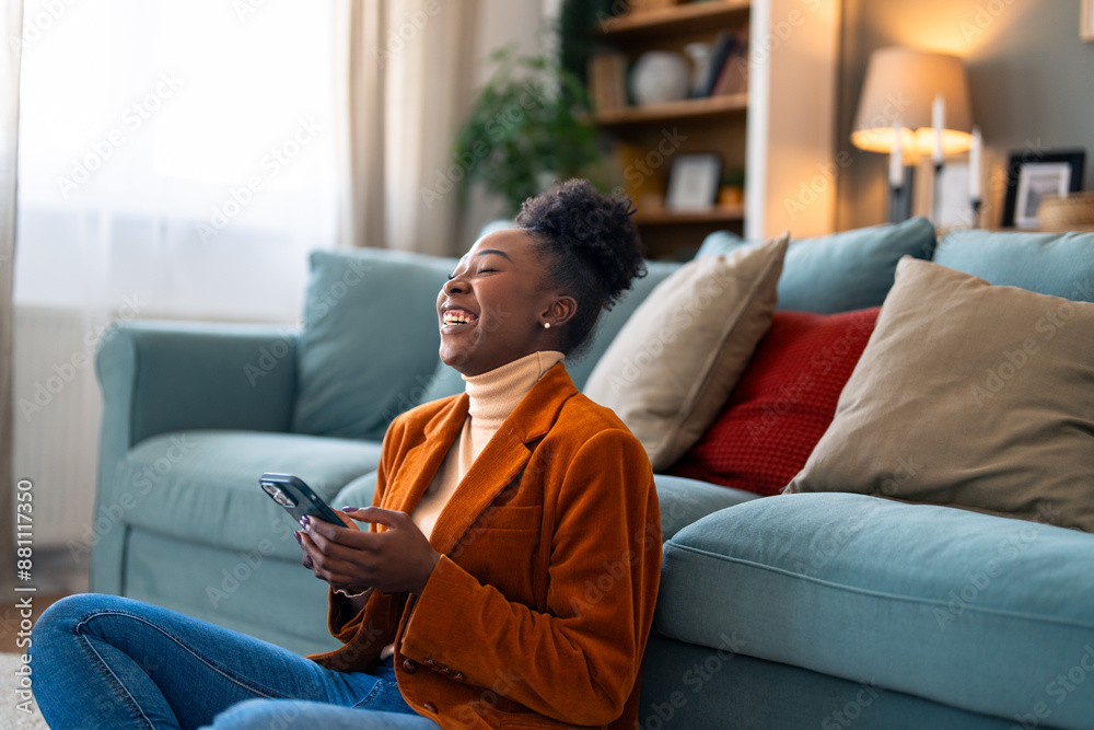 Beautiful black woman feeling very happy after reading a message on her smart phone. She is sitting on the floor in her apartment. Beautiful black woman feeling very happy after reading a message on her smart phone. She is sitting on the floor in her apartment.