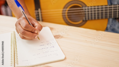 Fotografie A woman's hand writing lyrics in a notebook on a wooden table with an acoustic guitar in the background, indoors