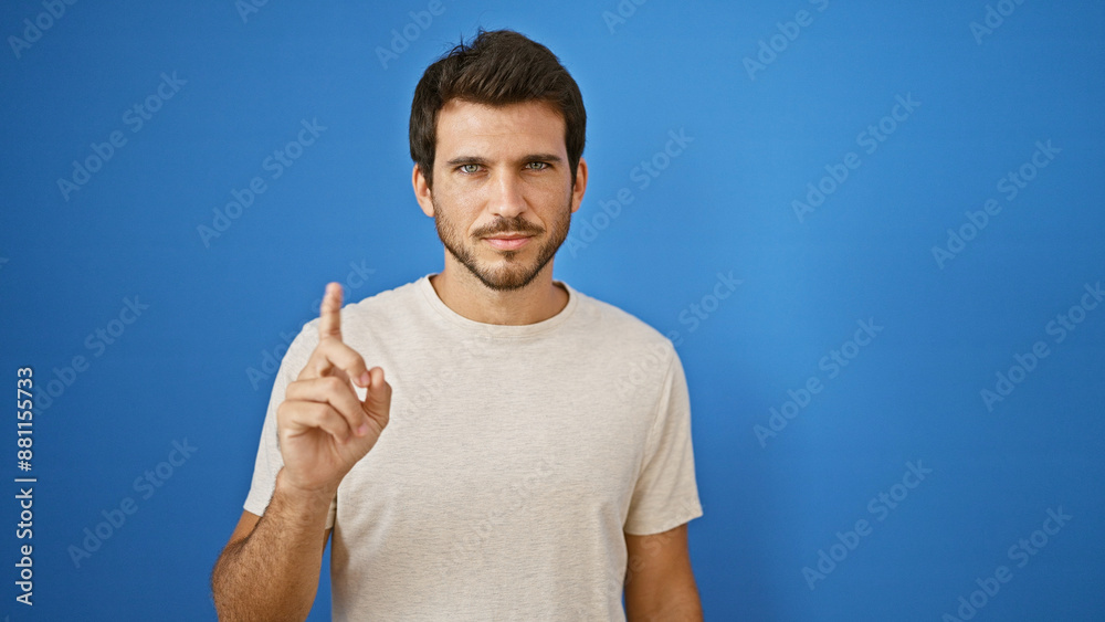 A young hispanic man with a beard gestures against a blue wall outdoors, exuding confidence and casual style. A young hispanic man with a beard gestures against a blue wall outdoors, exuding confidence and casual style.