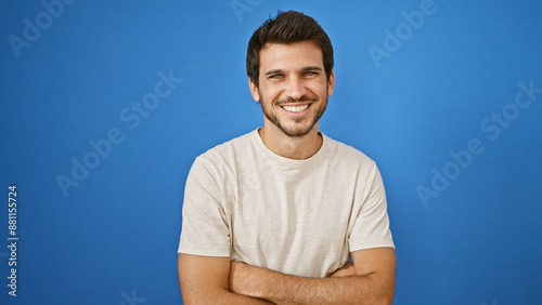 Smiling young hispanic man with beard standing with arms crossed against a blue background outdoors © Krakenimages.com