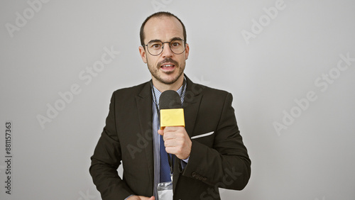 Hispanic man in suit holding microphone against white background portrays a professional speaker or reporter.