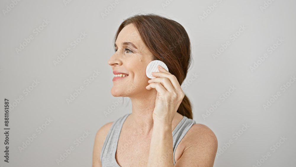 A smiling middle-aged woman gracefully applying makeup with a cotton pad against a white background, portraying cleanliness and beauty. A smiling middle-aged woman gracefully applying makeup with a cotton pad against a white background, portraying cleanliness and beauty.